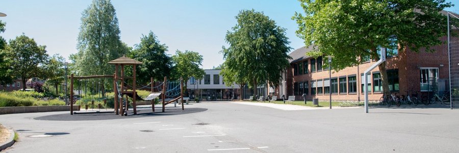 Schulhof der Eider Trenne Schule Tönning mit Bäumen, Klettergerüst und dem Schulgebäude im Hintergrund